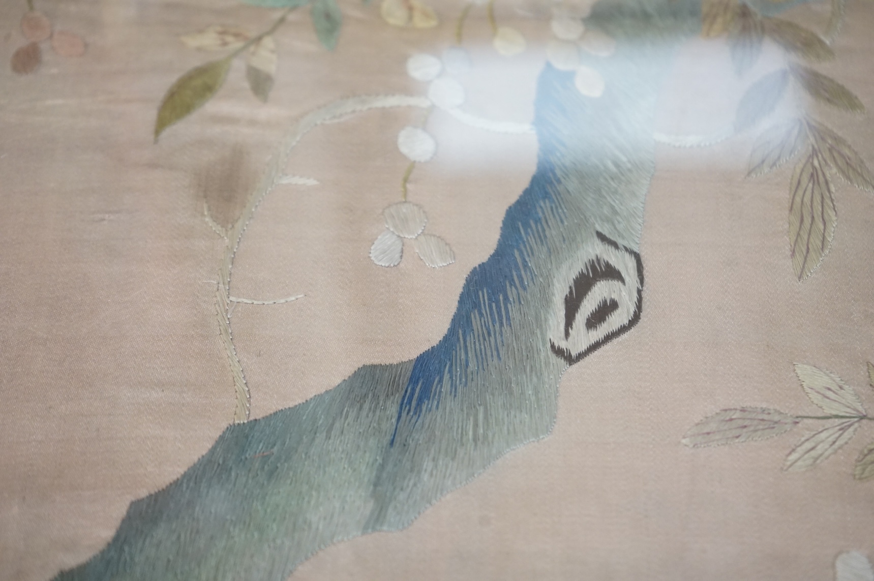 A pair of framed 19th century Chinese silk embroideries of exotic birds amongst entwined flowering branches, embroidered on a beige silk back ground, possibly cut from a larger embroidery. 47cm x 57cm., Condition - one f